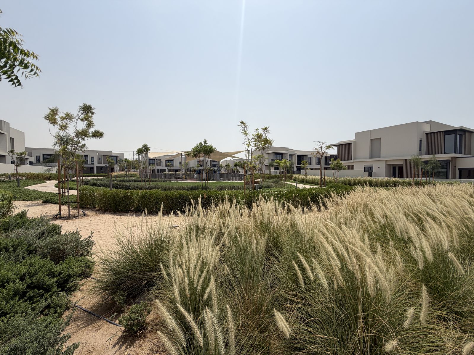 Community park with shaded play area and landscaping between townhouses in Jebel Ali Village, photographed September 2026